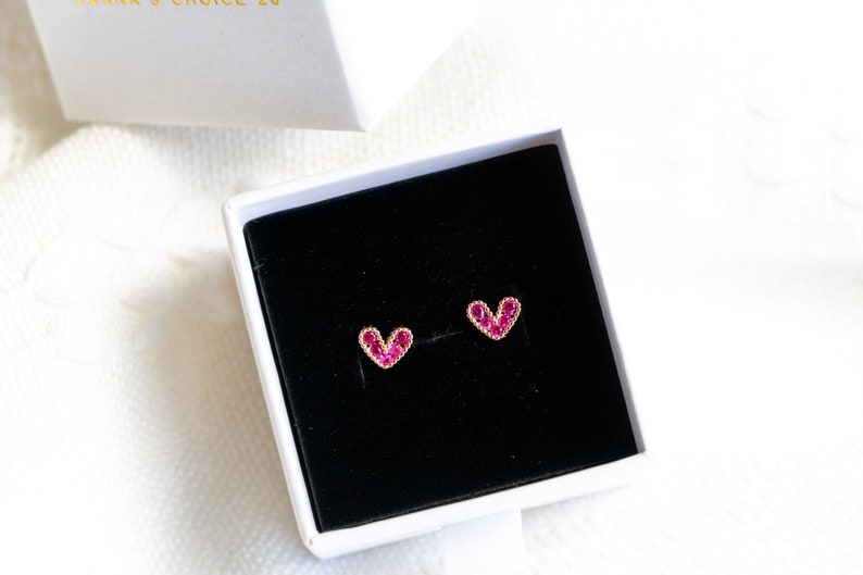 May include: A pair of heart-shaped earrings with pink gemstones set in gold.