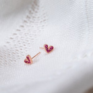 May include: A pair of rose gold heart-shaped earrings with small red gemstones.