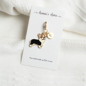May include: Gold charm featuring a black and white corgi with a gold heart charm. The charm is attached to a gold chain and is displayed on a white card with the text "hanna's choice" and "handmade with love".