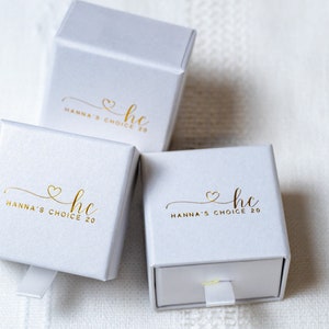 May include: Three white gift boxes with gold lettering. The boxes have a gold heart and the text "hc Hanna's Choice 20" on the front.