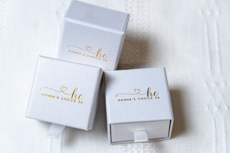 May include: Three white gift boxes with gold lettering. The boxes have a gold heart and the text "hc Hanna's Choice 20" on the front.