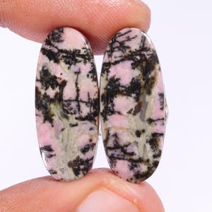 May include: Pair of oval-shaped pink and black gemstone cabochons. The stones have a unique dendritic pattern.