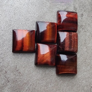 May include: A group of seven red tiger's eye gemstone cabochons, each with a square shape and a polished, glossy finish. The stones have a rich, reddish-brown color with a subtle chatoyancy effect.