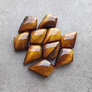 May include: A collection of ten faceted tiger's eye gemstones in a diamond shape. The stones are a rich golden brown colour with a slight sheen.