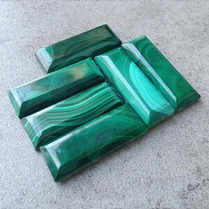 May include: Six polished malachite cabochons in various shades of green. The cabochons are rectangular and have a smooth, glossy finish.