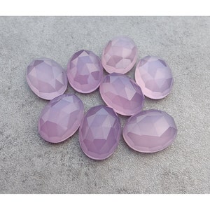 May include: Eight faceted oval-shaped gemstones in a pale lavender color. The stones are arranged in a cluster on a gray surface.