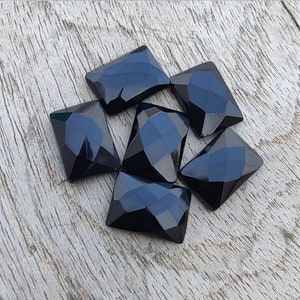 Op de afbeelding: Zes zwarte gefacetteerde edelsteen cabochons, gesneden in een rechthoekige vorm, gerangschikt op een houten oppervlak.