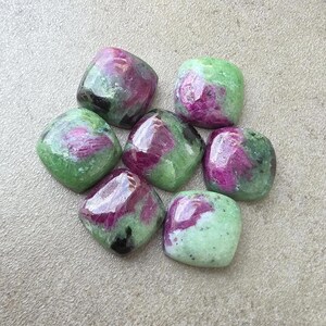 May include: Six polished, cushion-shaped cabochons featuring a mix of vibrant magenta-pink and mottled light green mineral patterns. Each stone displays a smooth, reflective surface with distinct colour variations and dark inclusions throughout.