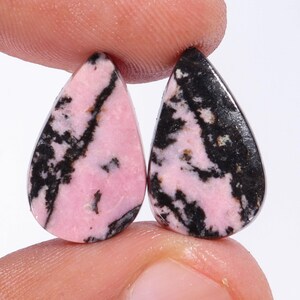 May include: Two teardrop-shaped pink and black gemstone cabochons. The stones have a swirling pattern of pink and black.