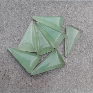 May include: Seven green triangle-shaped gemstone beads. The beads are translucent and have a light green color.