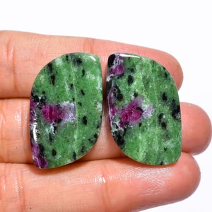 Könnte beinhalten: Zwei grüne, rosa und schwarze Edelstein-Cabochons mit einer glatten, polierten Oberfläche.