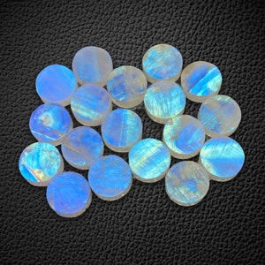 Op de afbeelding: Een verzameling ronde, iriserende maansteen cabochons. De stenen zijn licht wit met een blauwe glans. Ze zijn in een willekeurig patroon gerangschikt.