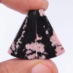 May include: Two triangular shaped cabochons of pink and black rhodochrosite, a semi-precious gemstone.