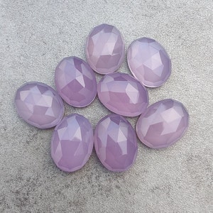 May include: Eight faceted oval-shaped gemstones in a pale lavender color. The stones are arranged in a loose circle on a gray background.