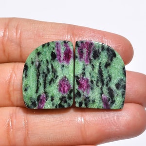 May include: Two green, black and pink gemstone cabochons with a rough, natural finish. The stones are cut in a half-round shape and have a mottled pattern.