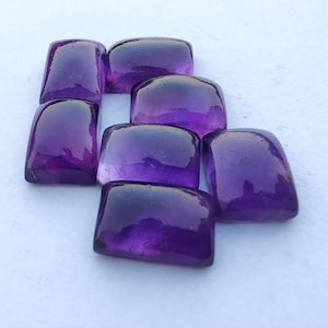 May include: A group of seven purple amethyst cabochons, cut and polished, with a smooth, glossy finish. The stones are arranged in a staggered pattern, showcasing their rich colour and natural beauty.