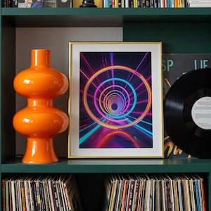 May include: An orange, double-bulb shaped decorative vase and a framed art print with a neon tunnel design are displayed on a green shelf. A black vinyl record is also on the shelf, along with a collection of vinyl records.