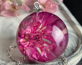 May include: A silver chain necklace with a round pendant featuring a pressed pink flower encased in clear resin.