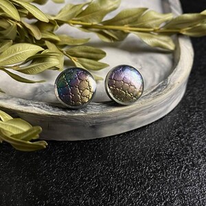 Peut inclure: Une paire de boucles d'oreilles rondes &agrave; clous iris&eacute;es avec un motif textur&eacute;. Les boucles d'oreilles sont sur une surface en marbre blanc.