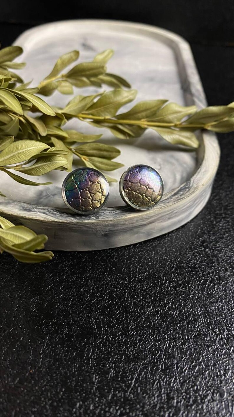 Peut inclure: Une paire de boucles d'oreilles rondes &agrave; clous iris&eacute;es avec un motif textur&eacute;. Les boucles d'oreilles sont sur une surface en marbre blanc.