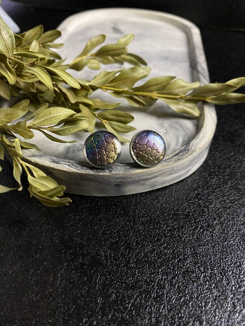Peut inclure: Une paire de boucles d'oreilles iris&eacute;es avec un motif textur&eacute; g&eacute;om&eacute;trique. Les boucles d'oreilles sont rondes et ont un dos argent&eacute;.