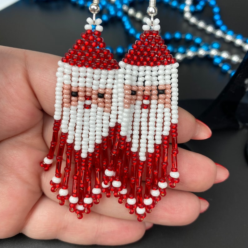 May include: Beaded Santa Claus earrings with red, white, and skin-tone beads. The earrings feature a Santa face design with a red hat and beard, white mustache, and skin-tone face. The earrings have a fringe of red beads.