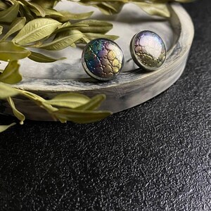 Peut inclure: Une paire de boucles d'oreilles rondes &agrave; clous iris&eacute;es avec une surface textur&eacute;e. Les boucles d'oreilles sont argent&eacute;es et ont une finition iris&eacute;e violet fonc&eacute;, verte et dor&eacute;e.