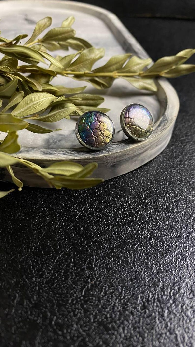 Peut inclure: Une paire de boucles d'oreilles rondes &agrave; clous iris&eacute;es avec une surface textur&eacute;e. Les boucles d'oreilles sont argent&eacute;es et ont une finition iris&eacute;e violet fonc&eacute;, verte et dor&eacute;e.