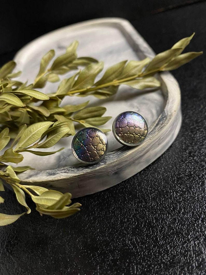 Peut inclure: Une paire de boucles d'oreilles rondes &agrave; clous iris&eacute;es avec une finition textur&eacute;e et m&eacute;tallique. Les boucles d'oreilles sont pr&eacute;sent&eacute;es sur un plateau en marbre blanc.