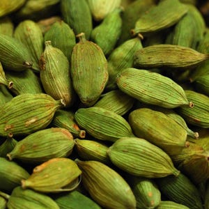 May include: Close-up of a pile of green cardamom pods. The pods are oval-shaped with a ridged texture and a light green color. The image is a close-up, showing the details of the pods.