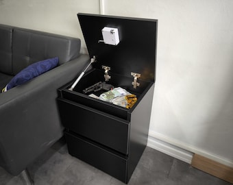 May include: A black bedside cabinet featuring two lower drawers and a top compartment that opens upwards using a gas strut hinge. Inside the top compartment, there is a handgun and a stack of paper currency. A white electronic lock is fixed inside.