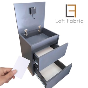 Pode incluir: Armário cinza com duas gavetas e um compartimento superior, com fechadura e dobradiças. Um cartão branco é segurado perto do armário. O logotipo "Loft Fabriq" é exibido no lado direito.
