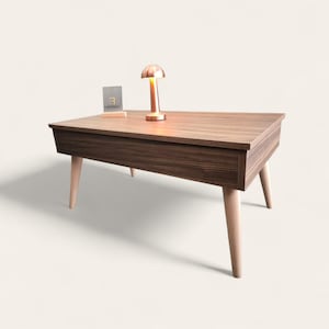 May include: A rectangular coffee table with a dark brown wood grain finish, featuring four light-colored tapered wooden legs. A small metallic lamp with a dome-shaped shade sits on the surface next to a small rectangular sign labeled Loft Fabric.