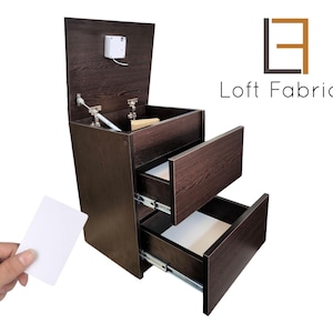 Pode incluir: Um armário de madeira castanha escura com duas gavetas e um compartimento superior. O armário tem um design moderno com um cartão branco sendo segurado em frente. O texto "Loft Fabriq" é exibido no lado direito.