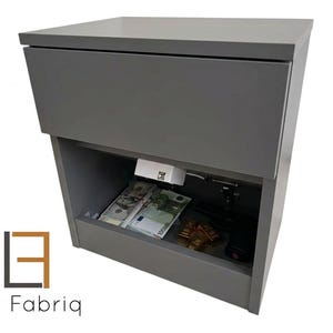 May include: A gray cabinet with a hidden compartment, containing cash, gold bars, and a handgun. The cabinet has a top drawer and an open lower section. The logo "Loft Fabriq" is visible on the bottom left.