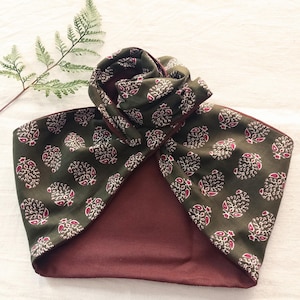 Può includere: Una fascia per capelli in stile turbante verde scuro con un motivo ripetuto di disegni floreali bianchi e rossi. L'interno è di colore bordeaux unito e la fascia è realizzata in tessuto morbido.