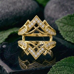 May include: A yellow gold ring guard featuring two chevron-shaped bands connected by side loops. The bands are encrusted with small, clear round-cut stones arranged in a V-pattern along the top and bottom edges of the open-center design.