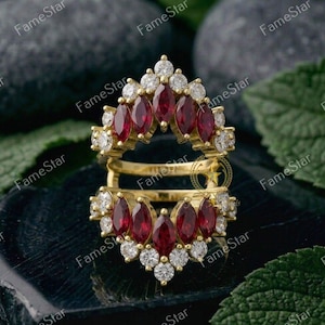 May include: A gold ring with a double band design. The ring is adorned with marquise-cut red gemstones and round white gemstones. The ring is set against a dark background with the text "FameStar" repeated.