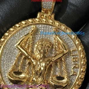 May include: Gold pendant with a detailed design of the Libra zodiac sign, featuring a woman holding scales. The pendant is covered in small, clear stones, giving it a sparkling effect.