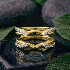 May include: A yellow gold ring guard featuring two curved bands connected at the sides. Each band has a V-shaped center section encrusted with small, clear, round-cut stones. The metal has a polished finish, and the design creates an open space.