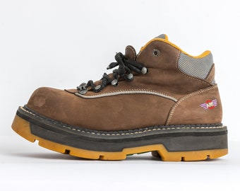 May include: Brown leather hiking boots with black laces and a yellow sole. The boots have a logo on the side that says "ART" with a winged design.