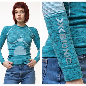 Puede incluir: Una camiseta de manga larga de color turquesa con un patrón blanco y turquesa. La camiseta tiene la palabra "X-BIONIC" impresa en la manga.