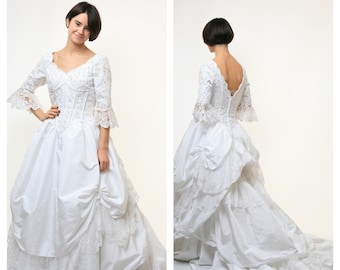 May include: A white wedding dress with lace detailing and a full skirt. The dress has a sweetheart neckline and three-quarter sleeves.