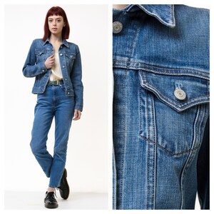 Puede incluir: Una chaqueta vaquera azul con cierre de botones, dos bolsillos en el pecho y un bolsillo único en el lado izquierdo. La chaqueta tiene un corte clásico y está hecha de una mezclilla suave y cómoda.