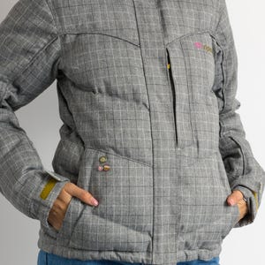 Puede incluir: Chaqueta de invierno gris con estampado de cuadros, capucha y ribete de piel sint&eacute;tica. La chaqueta tiene cremallera frontal, bolsillos y un peque&ntilde;o logotipo en el pecho. Los pu&ntilde;os tienen un acento amarillo.