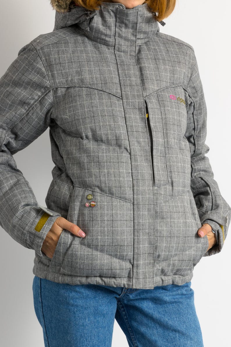 Puede incluir: Chaqueta de invierno gris con estampado de cuadros, capucha y ribete de piel sint&eacute;tica. La chaqueta tiene cremallera frontal, bolsillos y un peque&ntilde;o logotipo en el pecho. Los pu&ntilde;os tienen un acento amarillo.