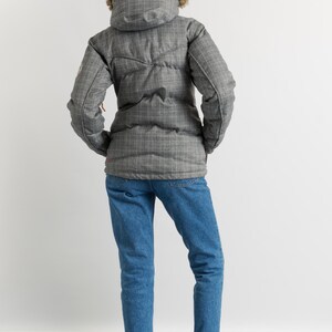 Puede incluir: Una chaqueta acolchada gris a cuadros con capucha forrada de piel, vaqueros azules y botines Chelsea burdeos. La chaqueta tiene un dise&ntilde;o acolchado y cierre de cremallera. Los vaqueros est&aacute;n doblados en los tobillos.