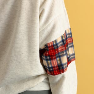 May include: A gray sweatshirt with a plaid patch on the sleeve. The plaid is red, blue, and white.