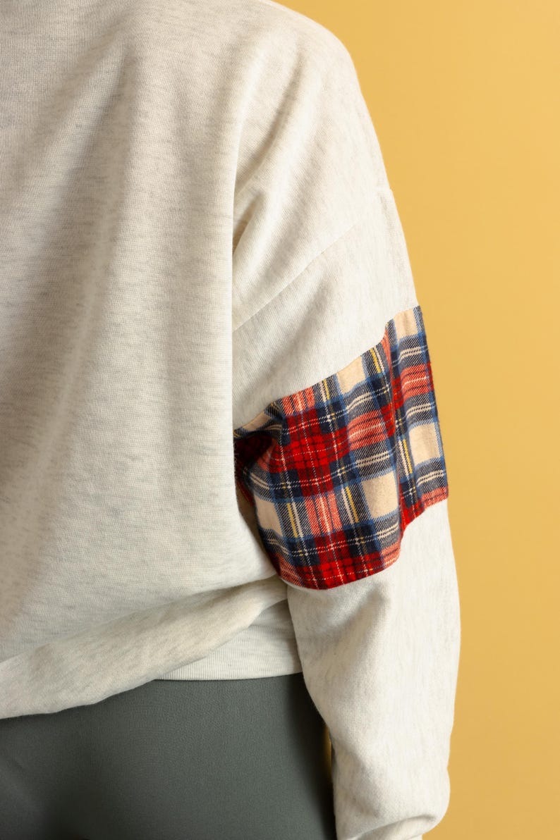 May include: A gray sweatshirt with a plaid patch on the sleeve. The plaid is red, blue, and white.