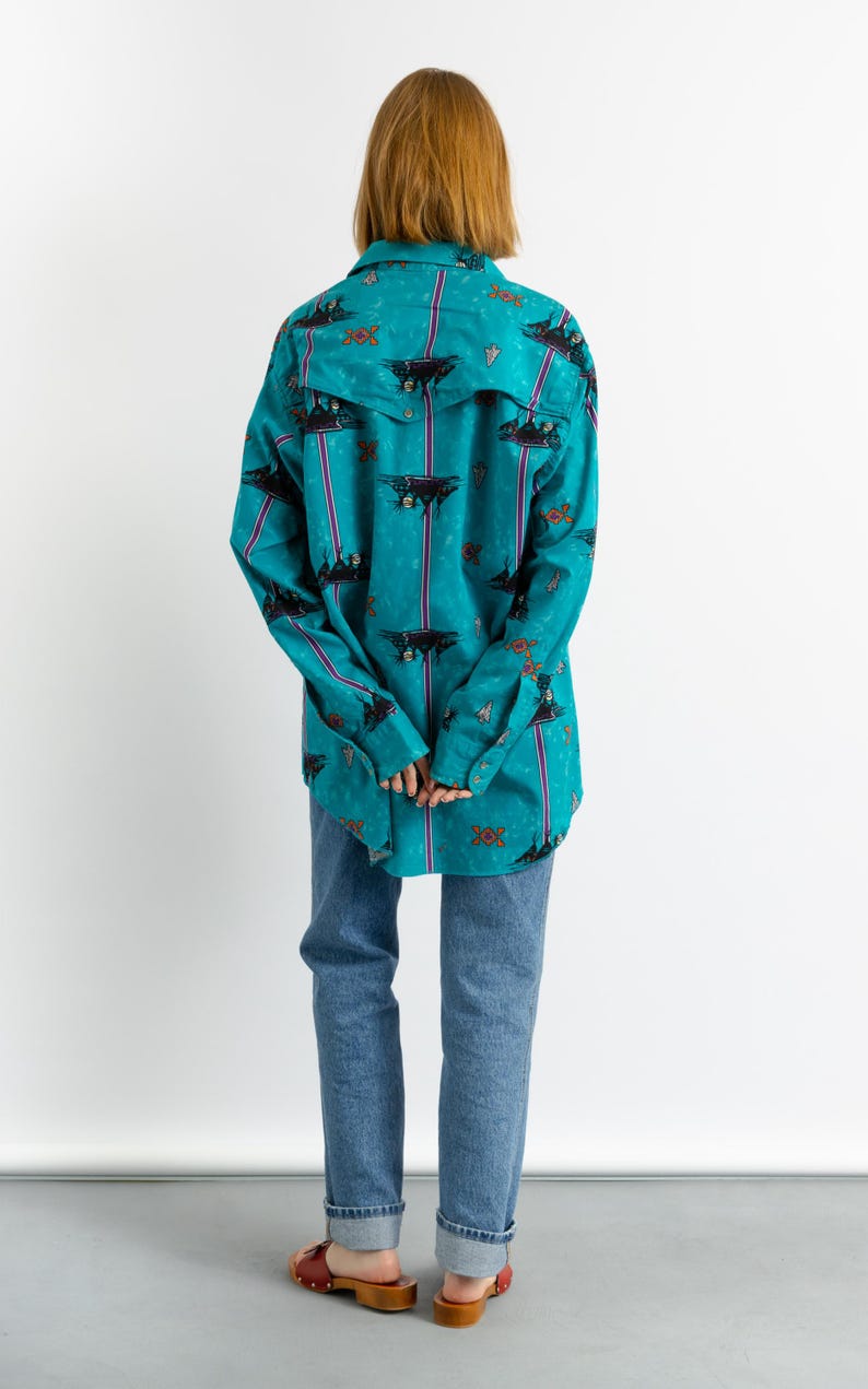 May include: A turquoise blue long-sleeved shirt with a colorful patterned design. The shirt has a button-down front and a relaxed fit.
